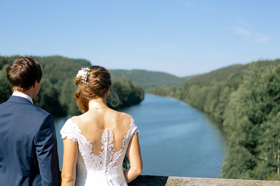 Das Brautpaar schaut auf eine Flusslandschaft in einem wäldlichen Tal.